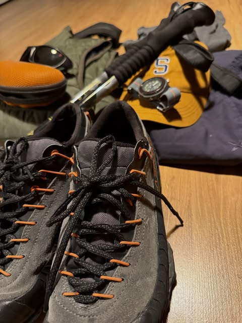 Grey hiking shoes with orange laces, a cap, and a compass