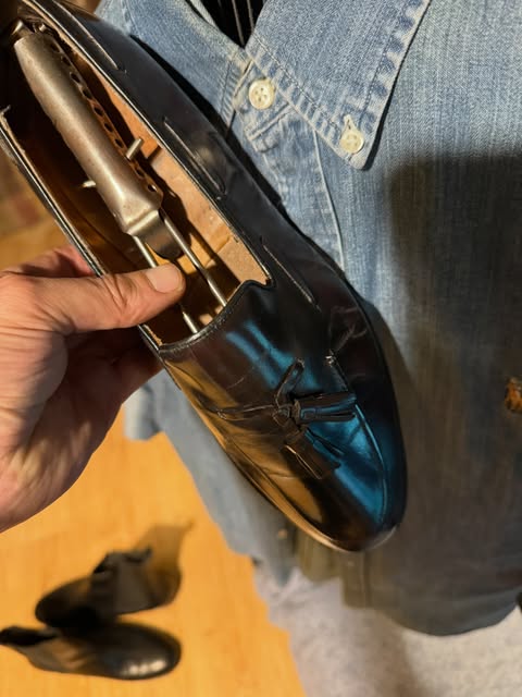 Black tassel loafer with a shoe tree, held in the hand