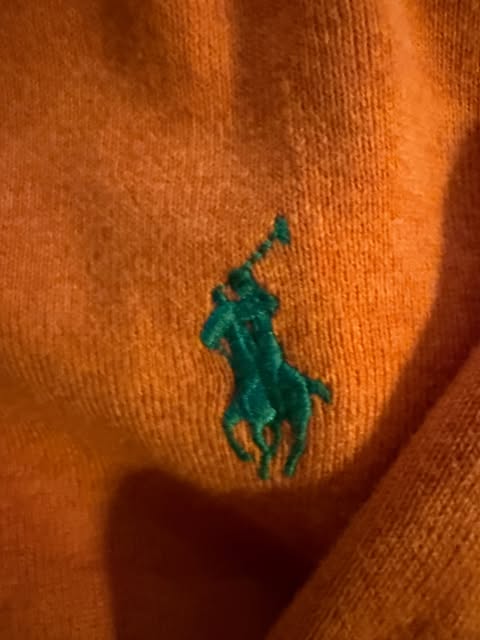 Close view of an orange knit with a green embroidered polo player